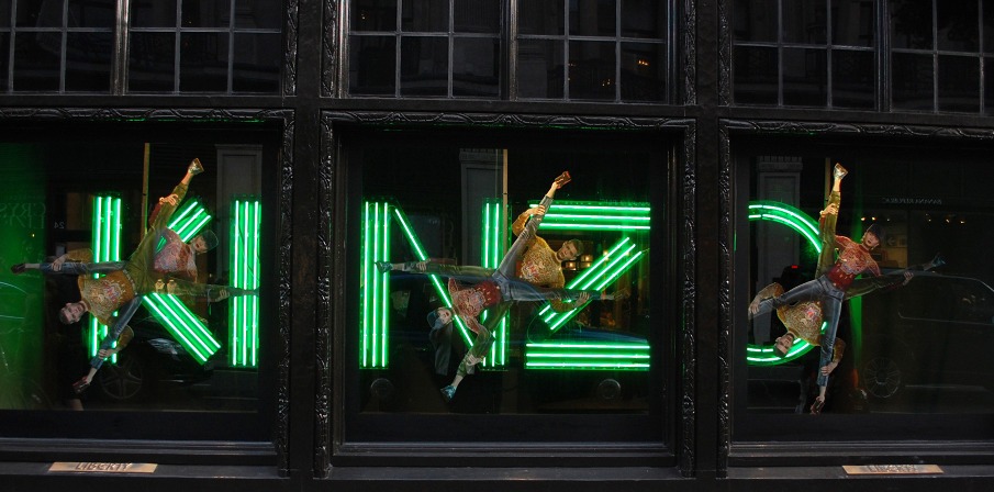 Letras de neón verde «KENZO» con figuras suspendidas en los escaparates de Liberty