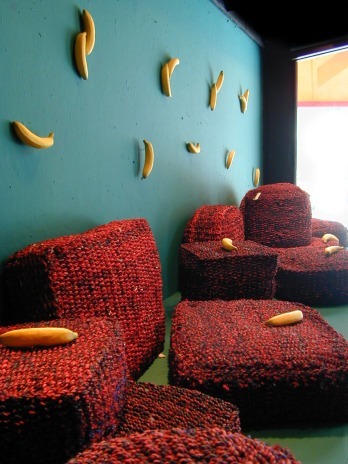Pared verde azulada con plátanos y sillones de punto rojo en un escaparate de Vinçon