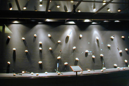 Pared oscura con relojes, cámaras y cuchillos iluminados como una colección en Vinçon