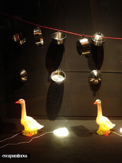 Ollas y sartenes colgadas sobre figuras de gansos iluminadas en un escaparate de Vinçon