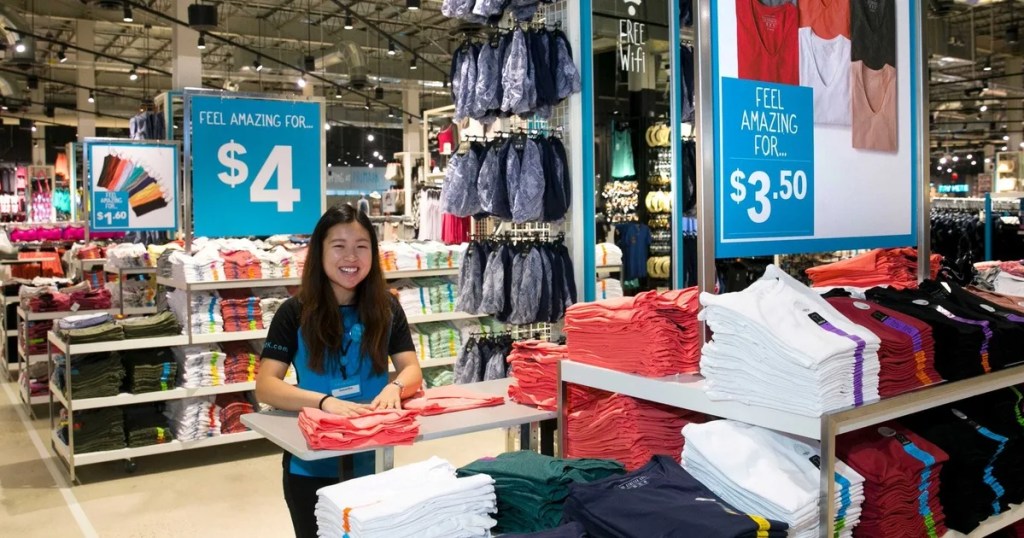 Low-cost store employee folding t-shirts next to signs for 4 and 3.50 dollars
