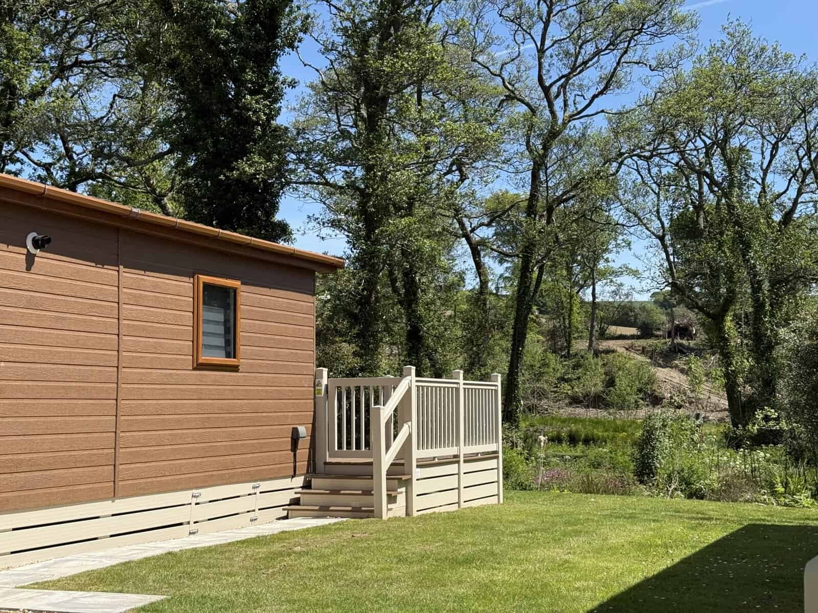 Brown cabin with white steps and railing, overlooking a wooded area.