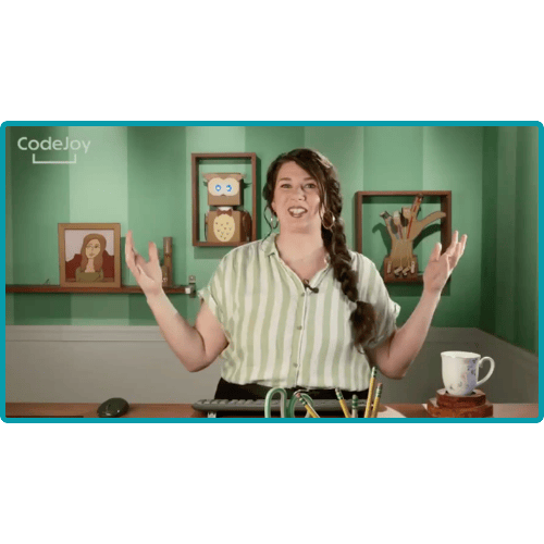 A woman with long hair, wearing a light-colored shirt, is speaking while gesturing in a brightly decorated room with framed pictures and a plant on the table.