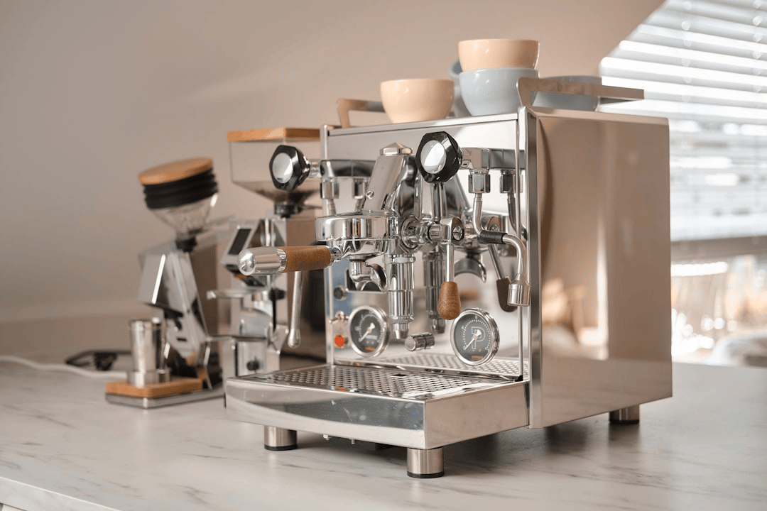 A stainless-steel espresso machine and hopper grinder on a light marble kitchen counter