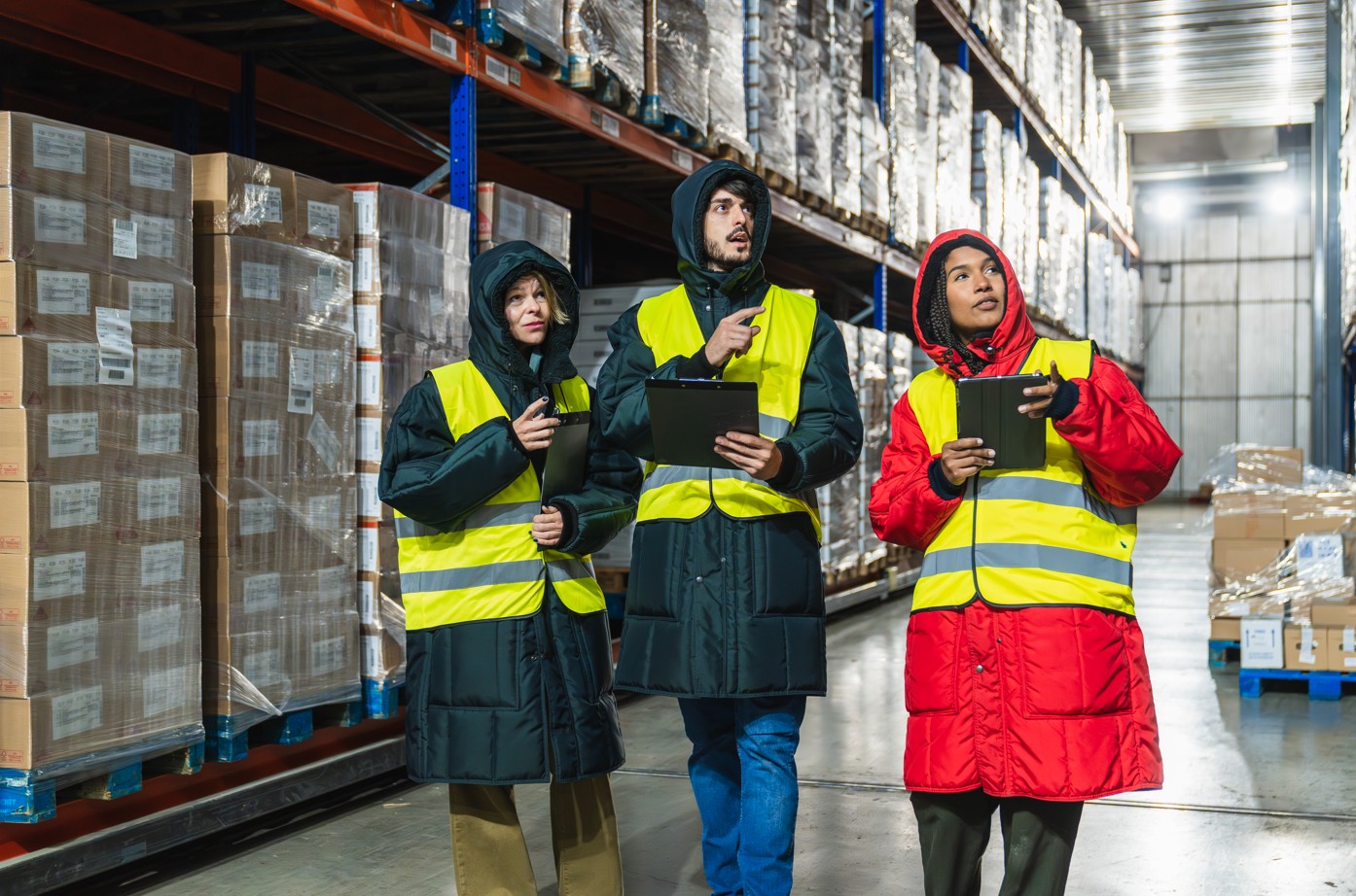 A team of 3 people walking through a refrigerated warehouse aisle auditing inventory on racks