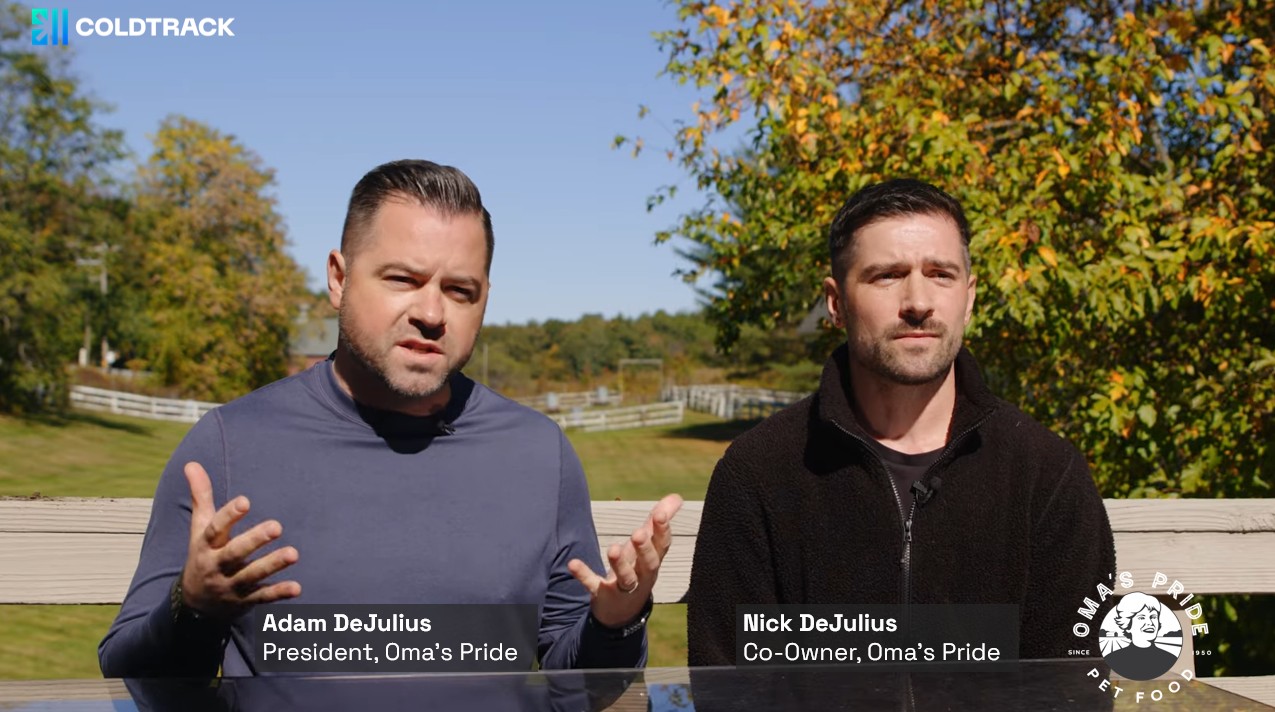 Adam and Nick DeJulius sit at a table outside with trees in the background showing the first signs of fall