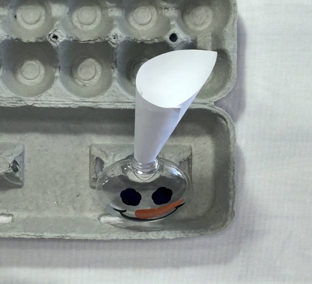 Photo showing how I use the egg carton to stabilize my ornament while adding the fake snow with a paper funnel.