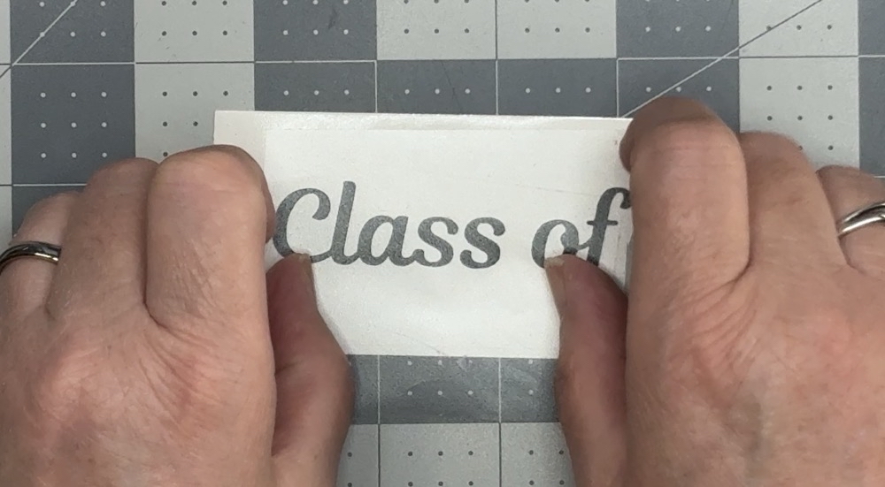 Screen shot showing the application of a small piece of Medium Tack Transfer tape to the “Class of” text for today’s 2026 Graduation Gift Card Holder project.