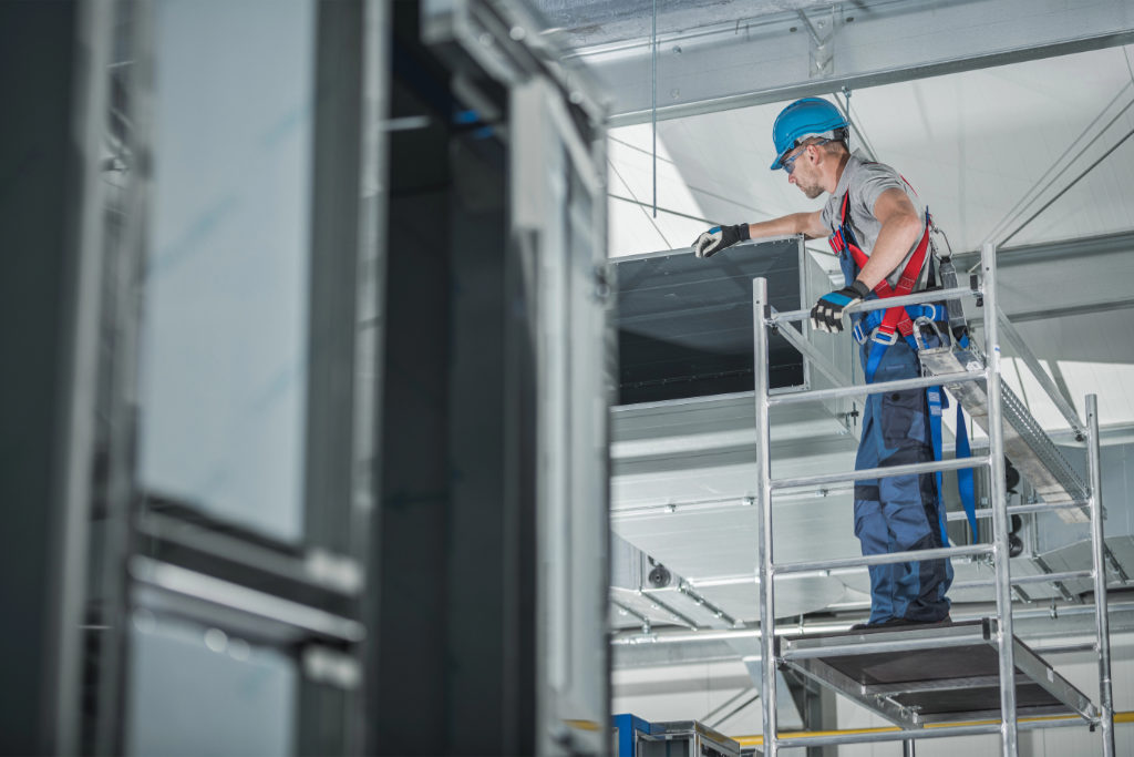 Image of an HVAC technician installing equipment on a scaffold at a worksite, featuring Comfort Conditioning and highlighting professional HVAC installation services in commercial settings.