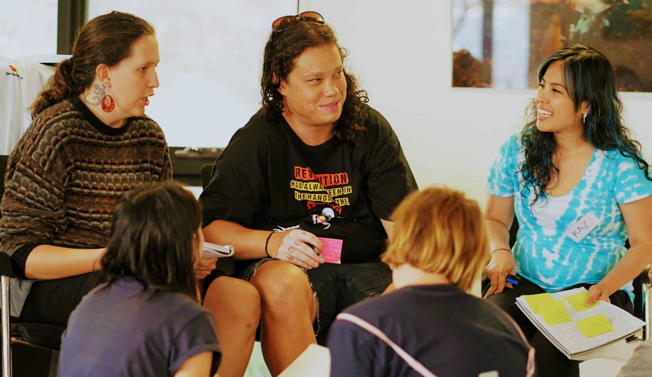Five people sit together in a workshop breakout group. They are smiling and talking to each other.