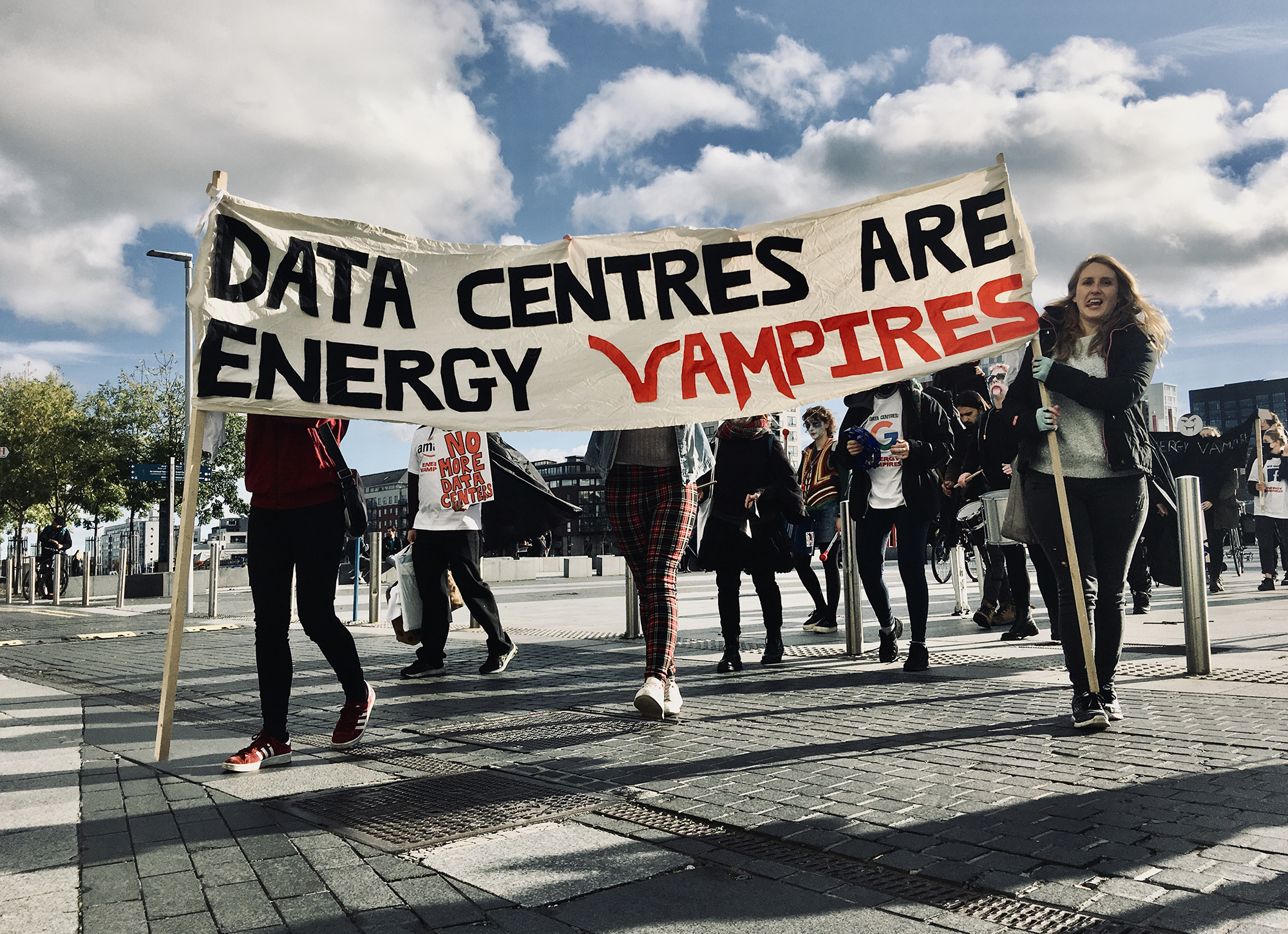 A group of people walk across a road carrying a large banner which reads 'Data Centres are Energy Vampires'