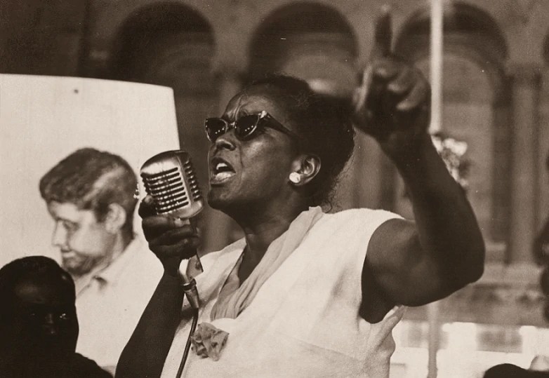 Ella Baker holds up a microphone and gives a speech in 1964.