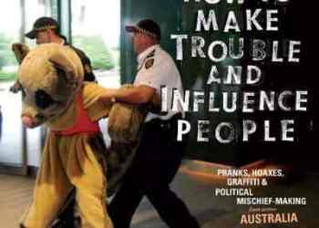 Cover of How to Make Trouble and Influence People. Features a photograph of someone in a sugar glider outfit being removed from an area by two policeman.