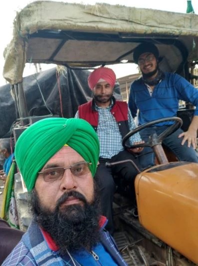 Three farmers stand in or next to a tractor during a protest in India.