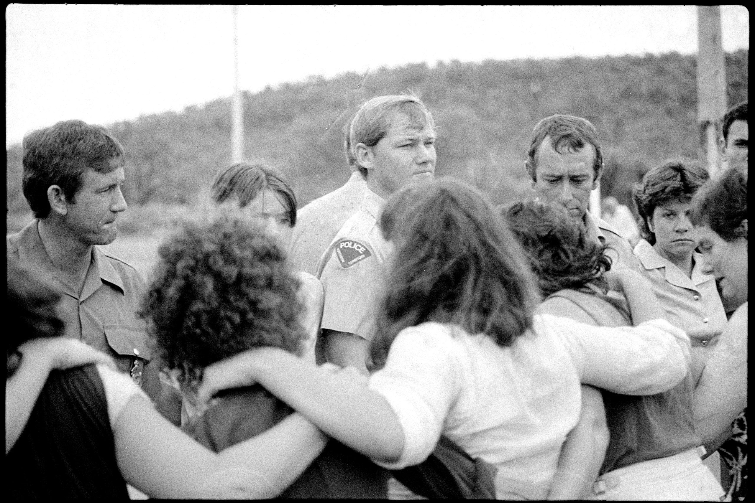 Women standing in a line of protest with there arms around each other facing off with a line of male policemen.