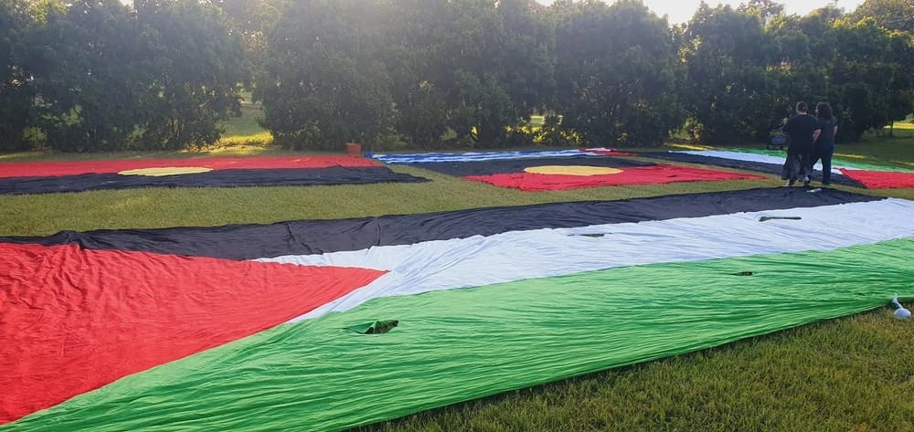 A huge Palestine flag lying on lawn in a park with Aboriginal flags in the background.