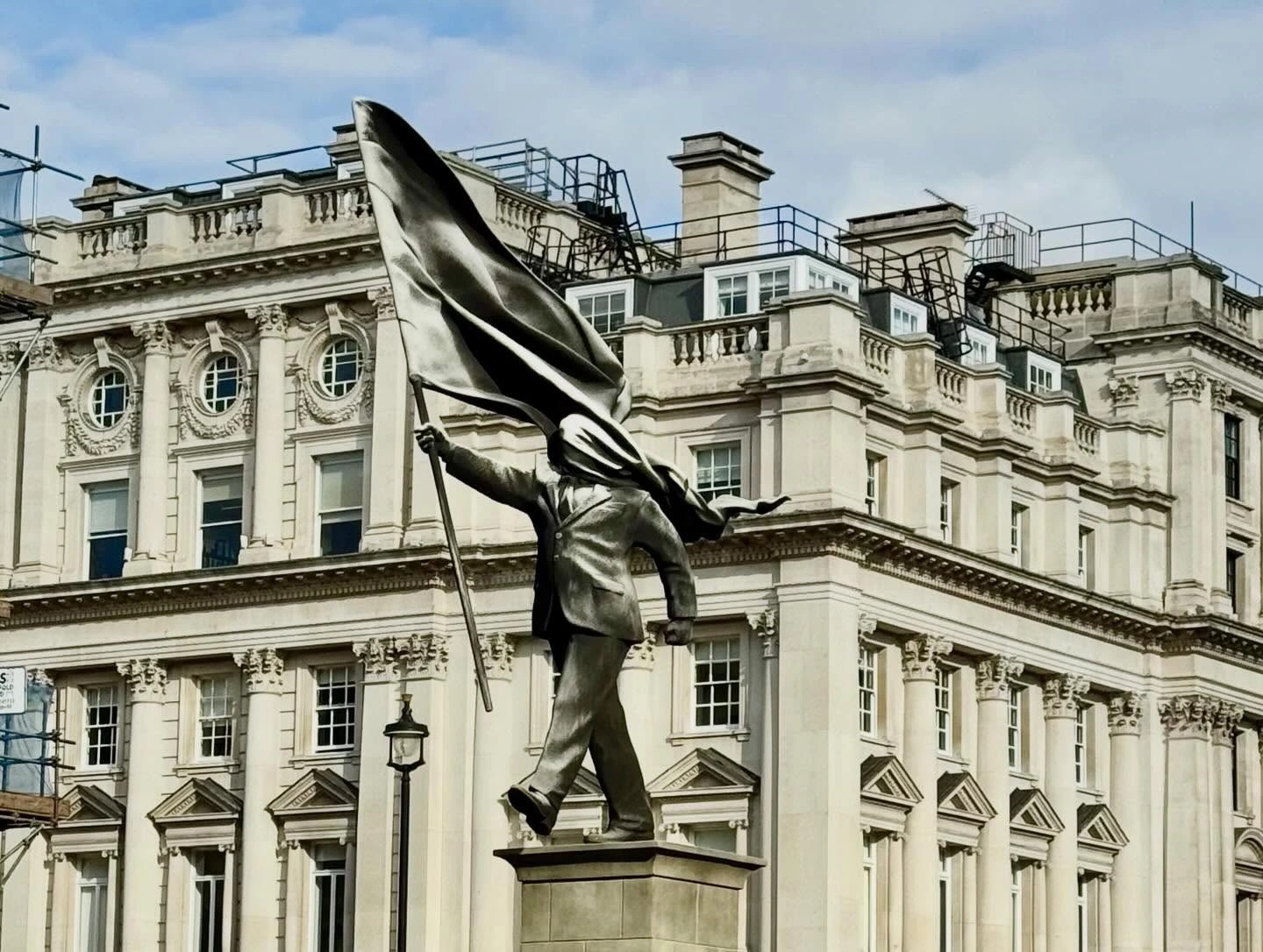 Photograph of a statue: A figure holds a large flag, the material wraps around their head so they can't see.
