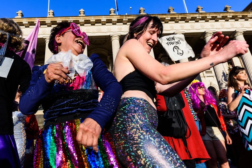 Extinction Rebellion members in disco outfits dance outside of the Victorian Parliament.