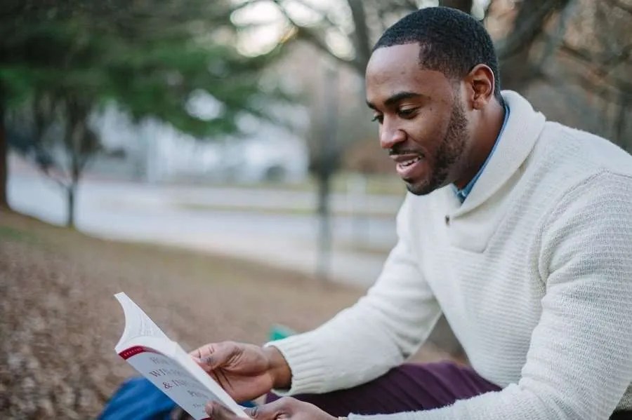 Man reading a book sat on a park bench