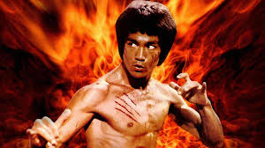 Un hombre sin camiseta en pose de artes marciales con arañazos en el pecho se sitúa frente a un fondo ardiente, evocando la legendaria energía de CÓMO MURIÓ BRUCE LEE.