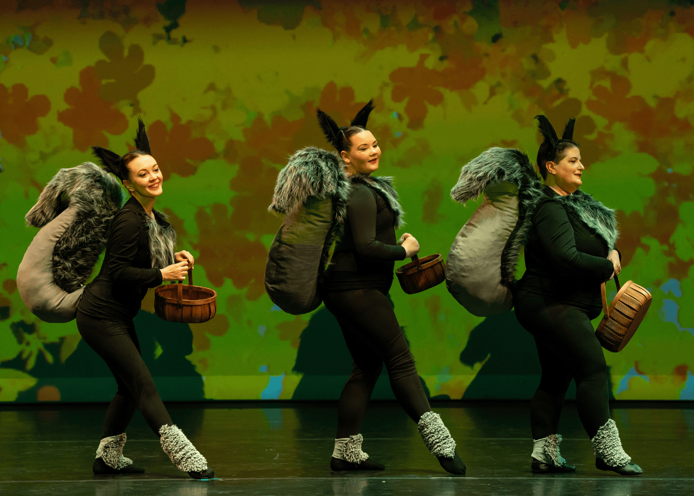 three dancers onstage dressed as squirrels holding baskets of acorns