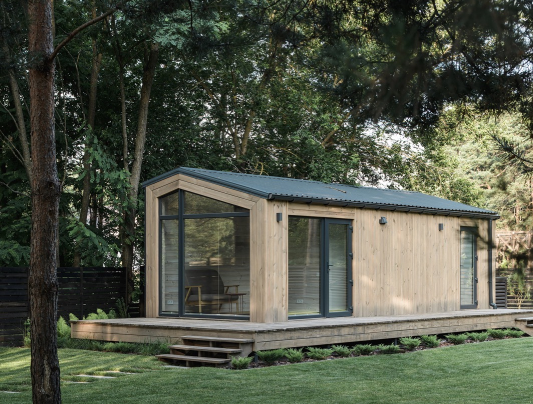 tuinhuis van hout met veel grote ramen en glas in grote tuin met terras.