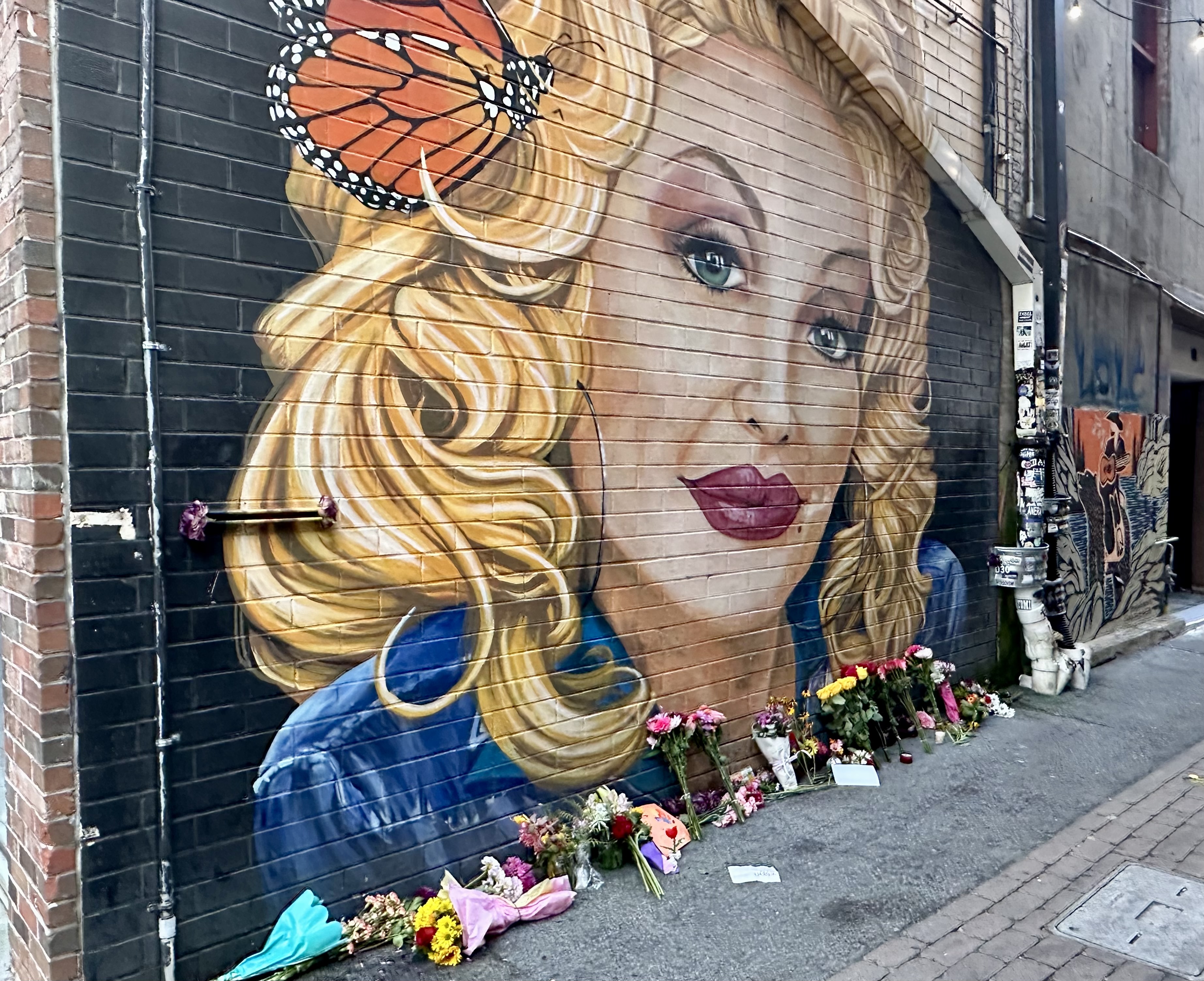 Mural of Dolly Parton in downtown Knoxville with flowers in front of it