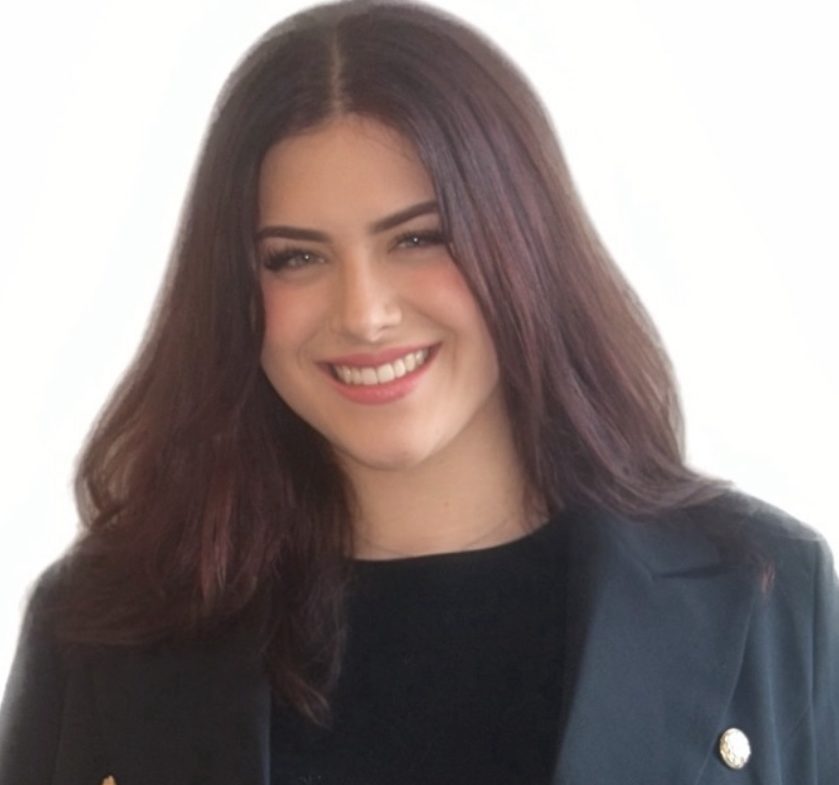 A smiling woman with long dark hair, wearing a black blazer with gold buttons, against a white background.