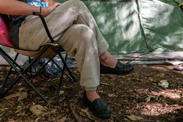 In a remote part of the D.C. woods, Meghann Abraham sits in a camping chair beside her tent.