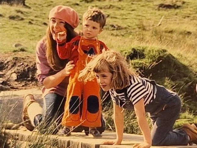 Toddler with mom and young child look over a wooden bridge on a trail in the mountains