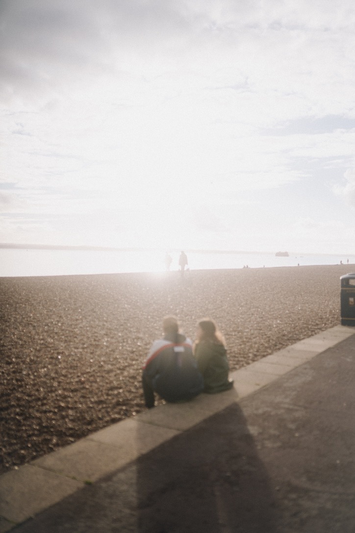 a couple sitting on the edge of the beach with the sun behind them, shot with the 1/4 tiffen promist