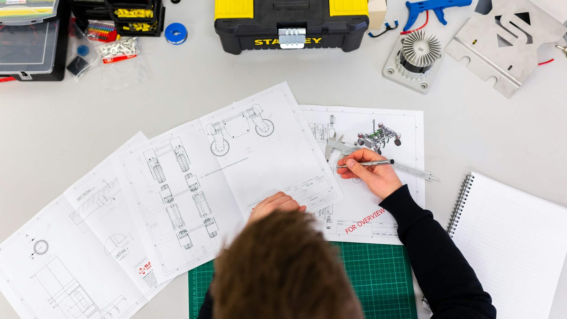 Engineer using a caliper to measure technical drawings on a desk