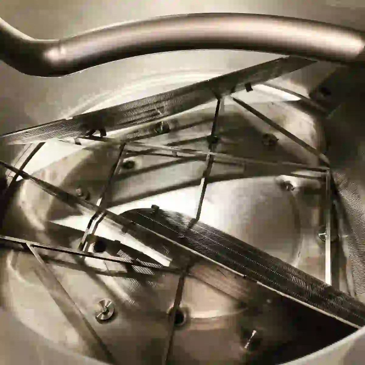 Inside a stainless steel mash tun, showing the stirring arms and grates