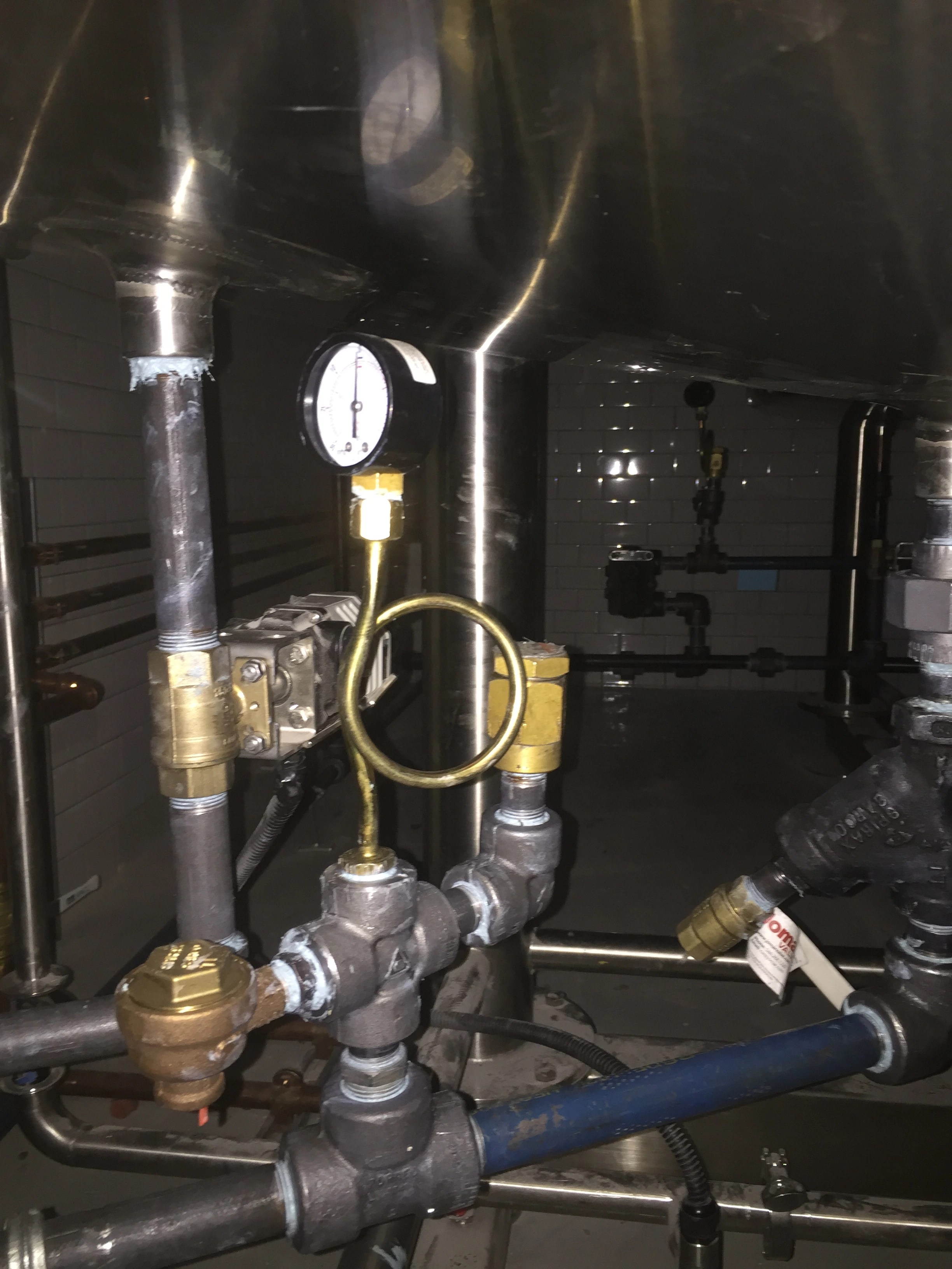 Pressure gauge on a siphon loop, actuated valve and black iron piping beneath a stainless vessel.