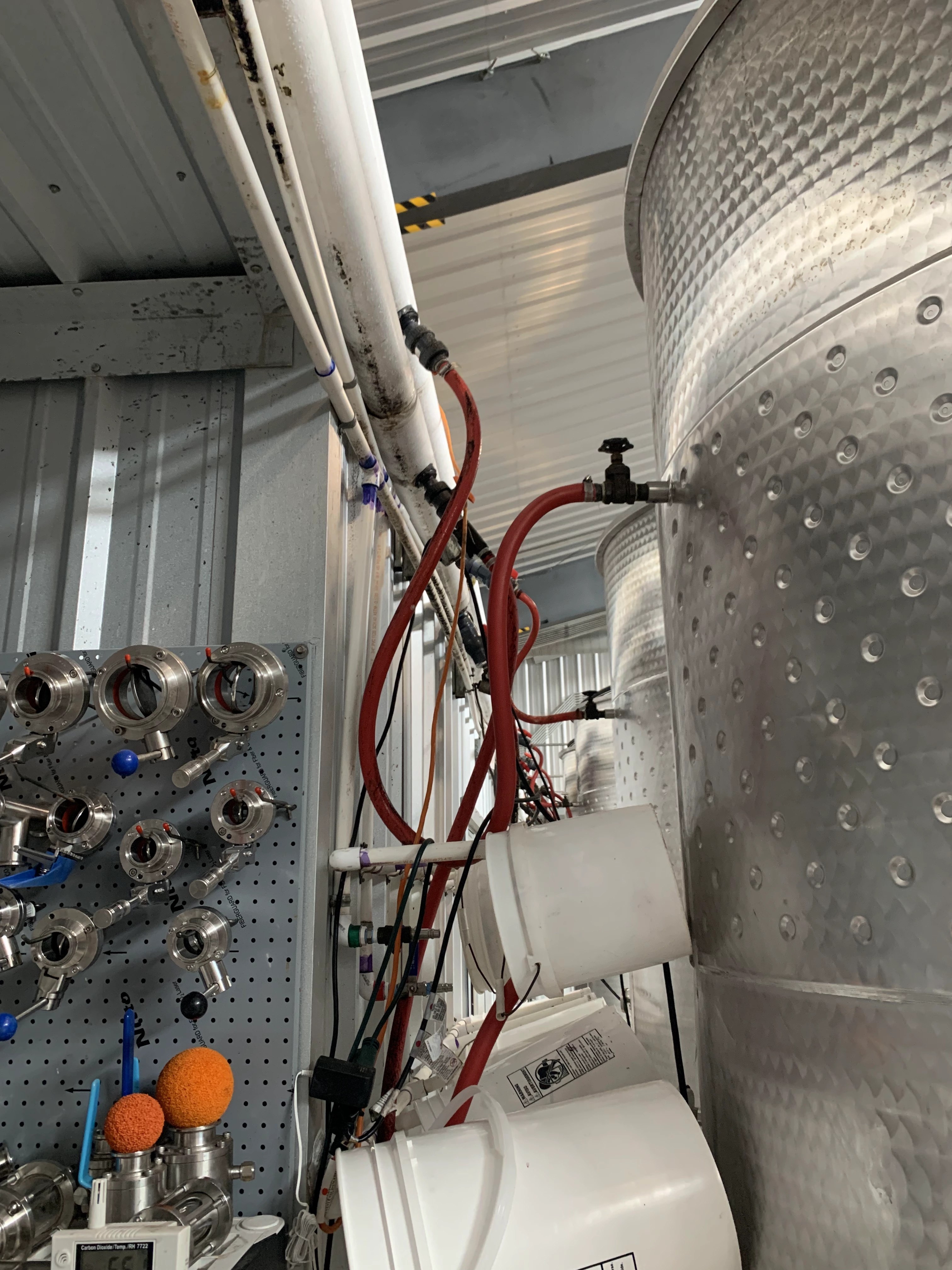 Dimple-jacketed stainless wine tank fed by red hoses from a wall-mounted glycol manifold