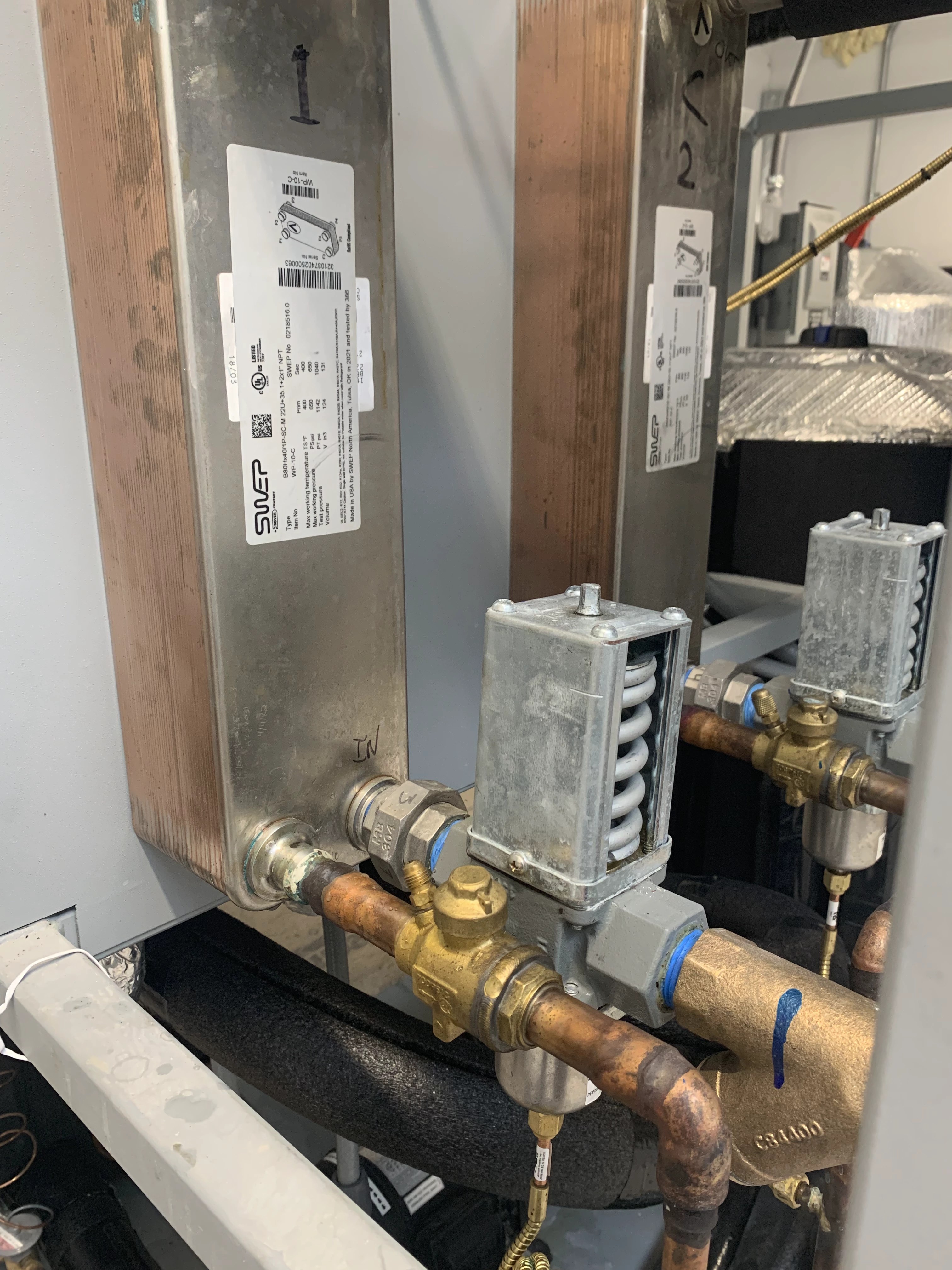 Refrigeration pressure controls, brass valves and copper piping beside plate heat exchangers on a chiller skid