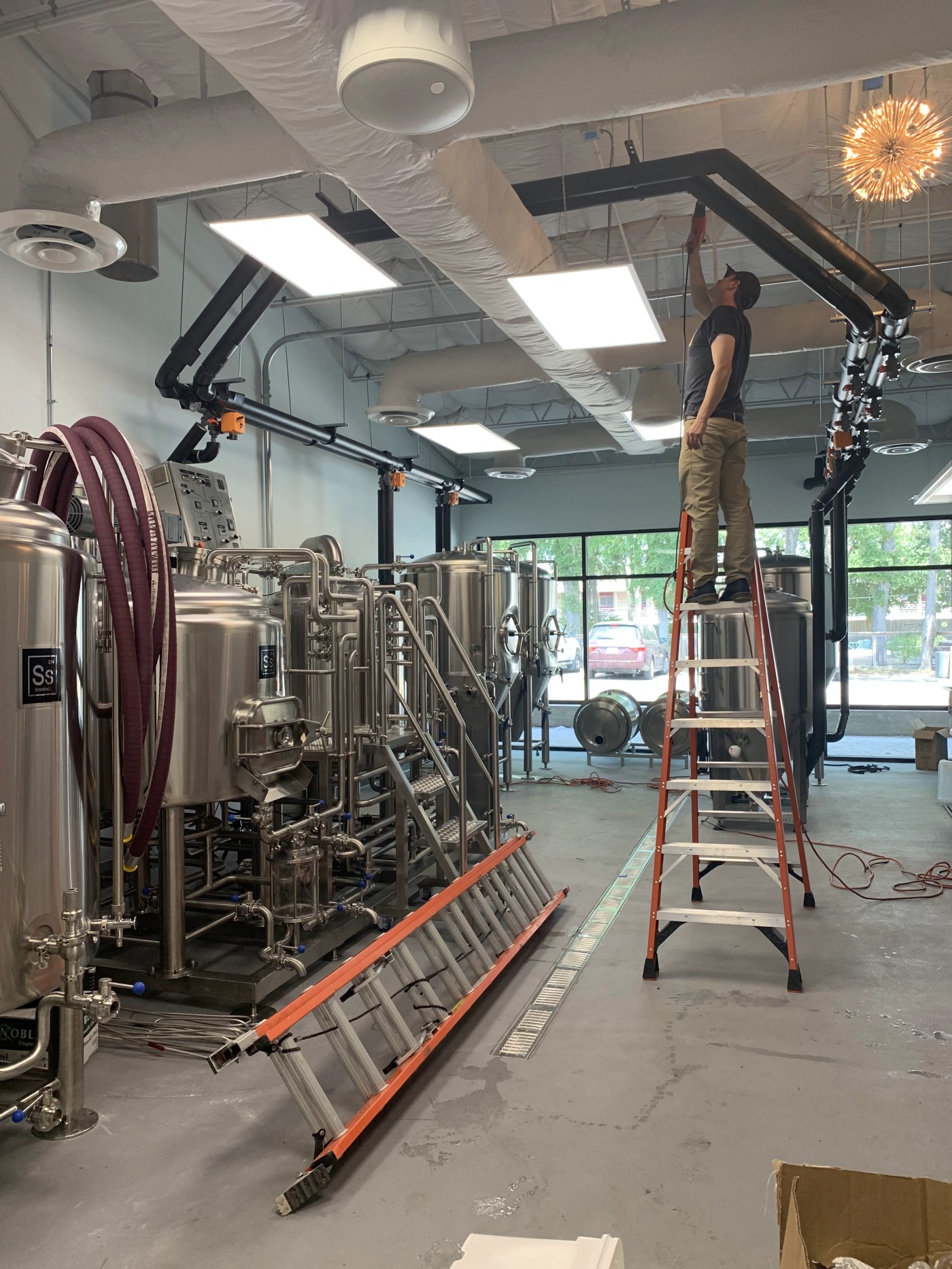 People working from ladders on overhead piping beside stainless steel tanks