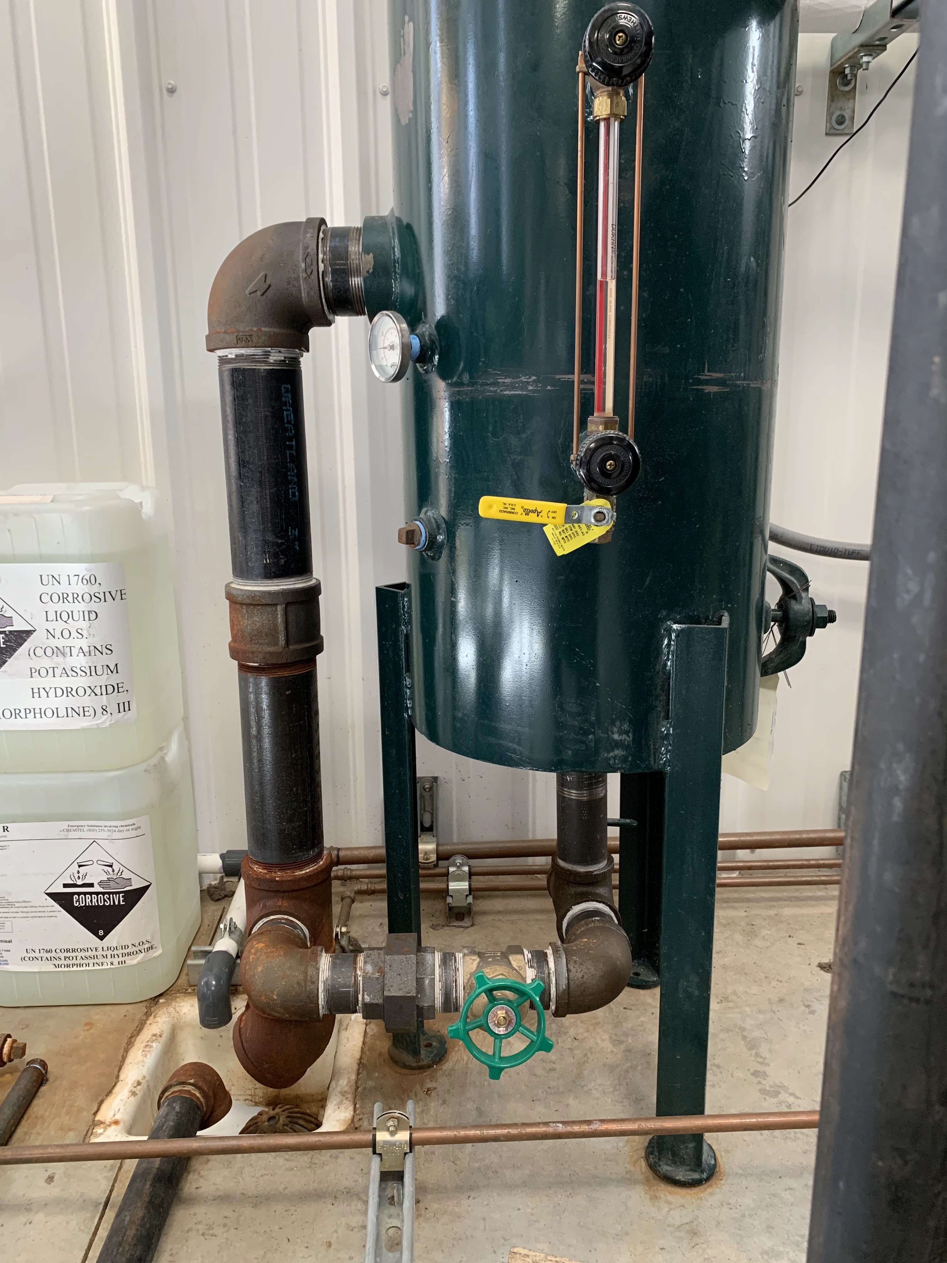 Dial thermometer and sight-glass level gauge on a green vessel with black iron piping and valves.