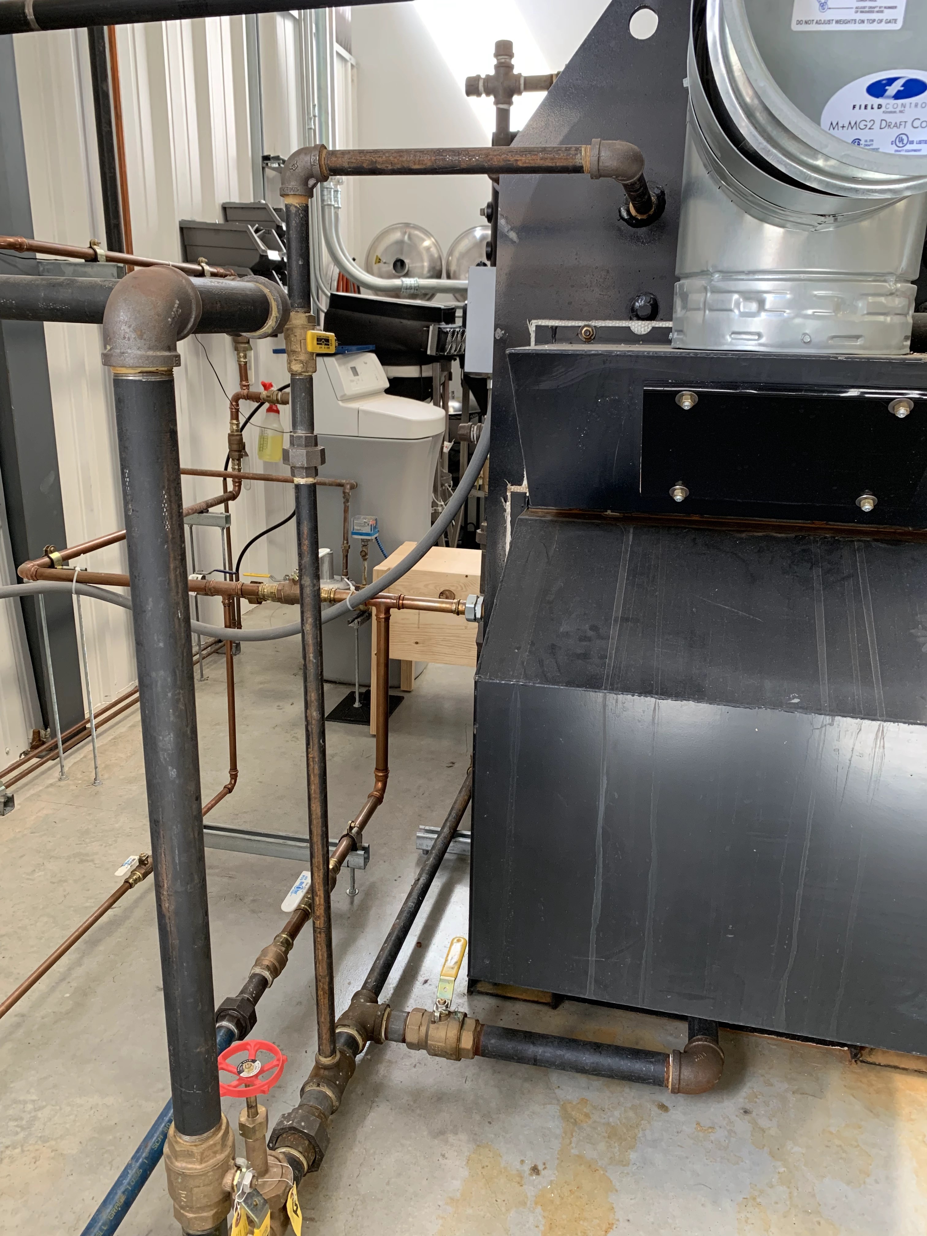 Boiler with draft control, black iron piping, gas valves and electrical conduit in a utility room.