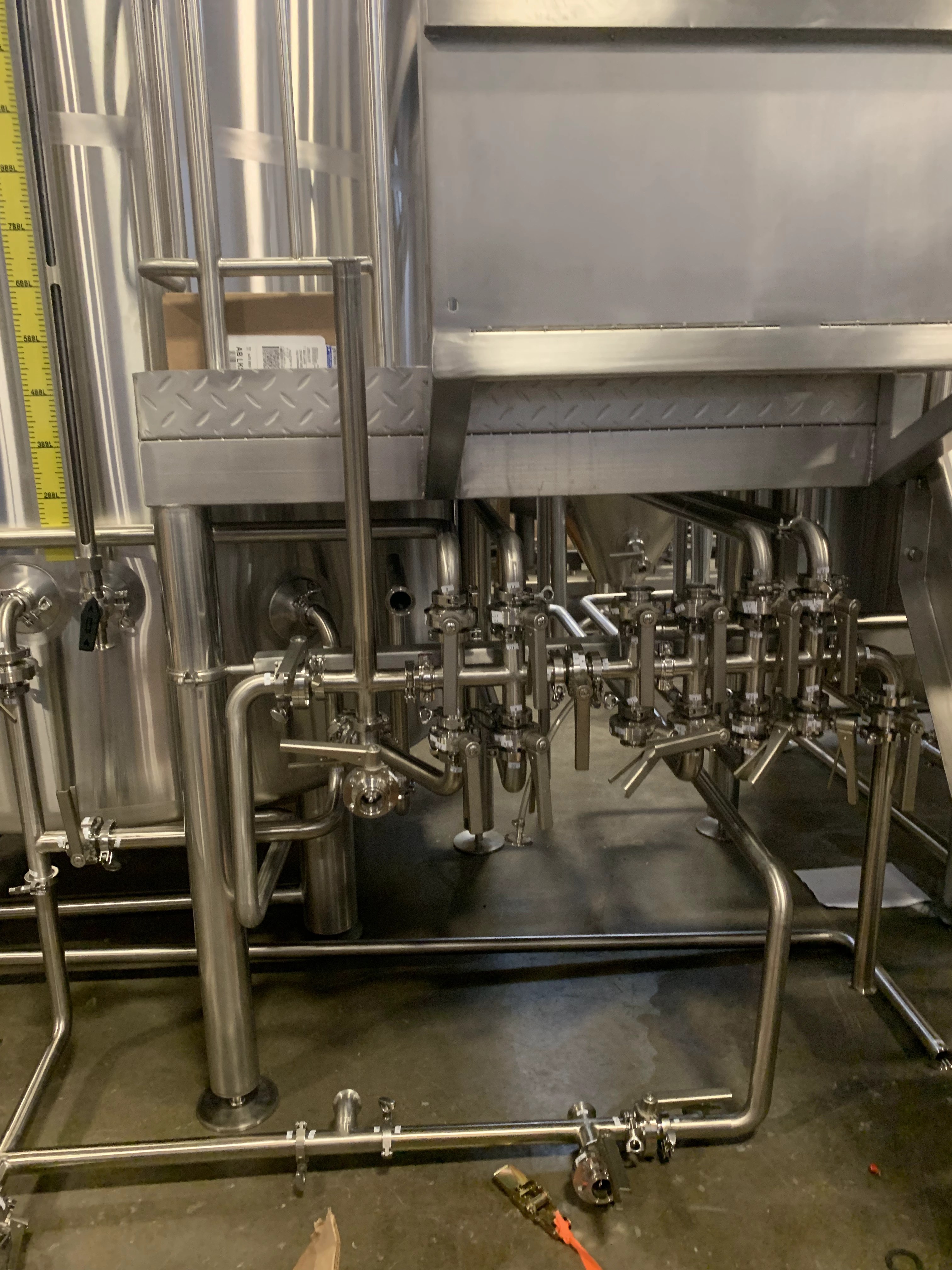 Stainless valve manifold with sanitary butterfly valves beneath a brewhouse work platform
