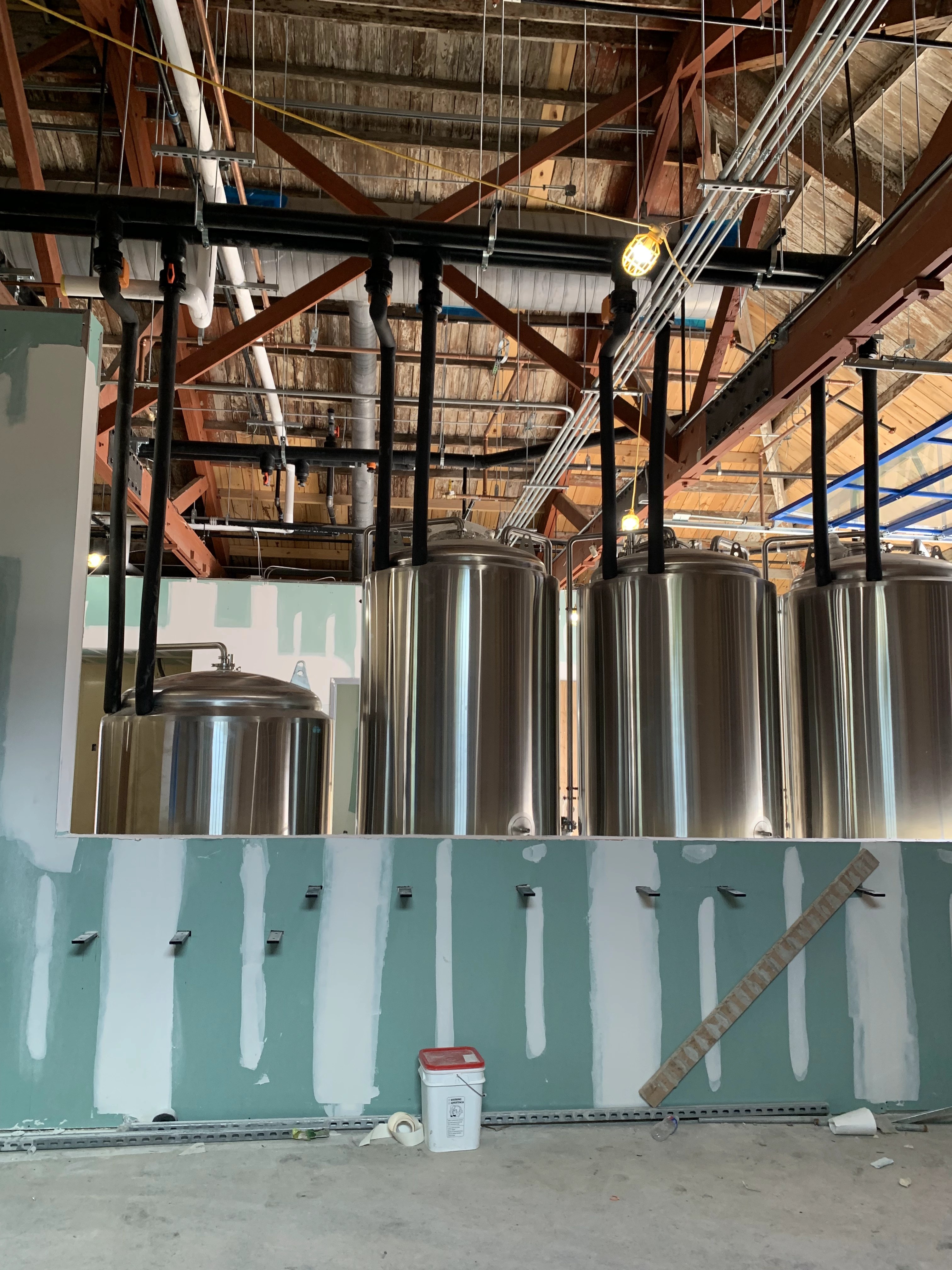 Stainless tanks with insulated lines dropping from an overhead header during a brewery build-out