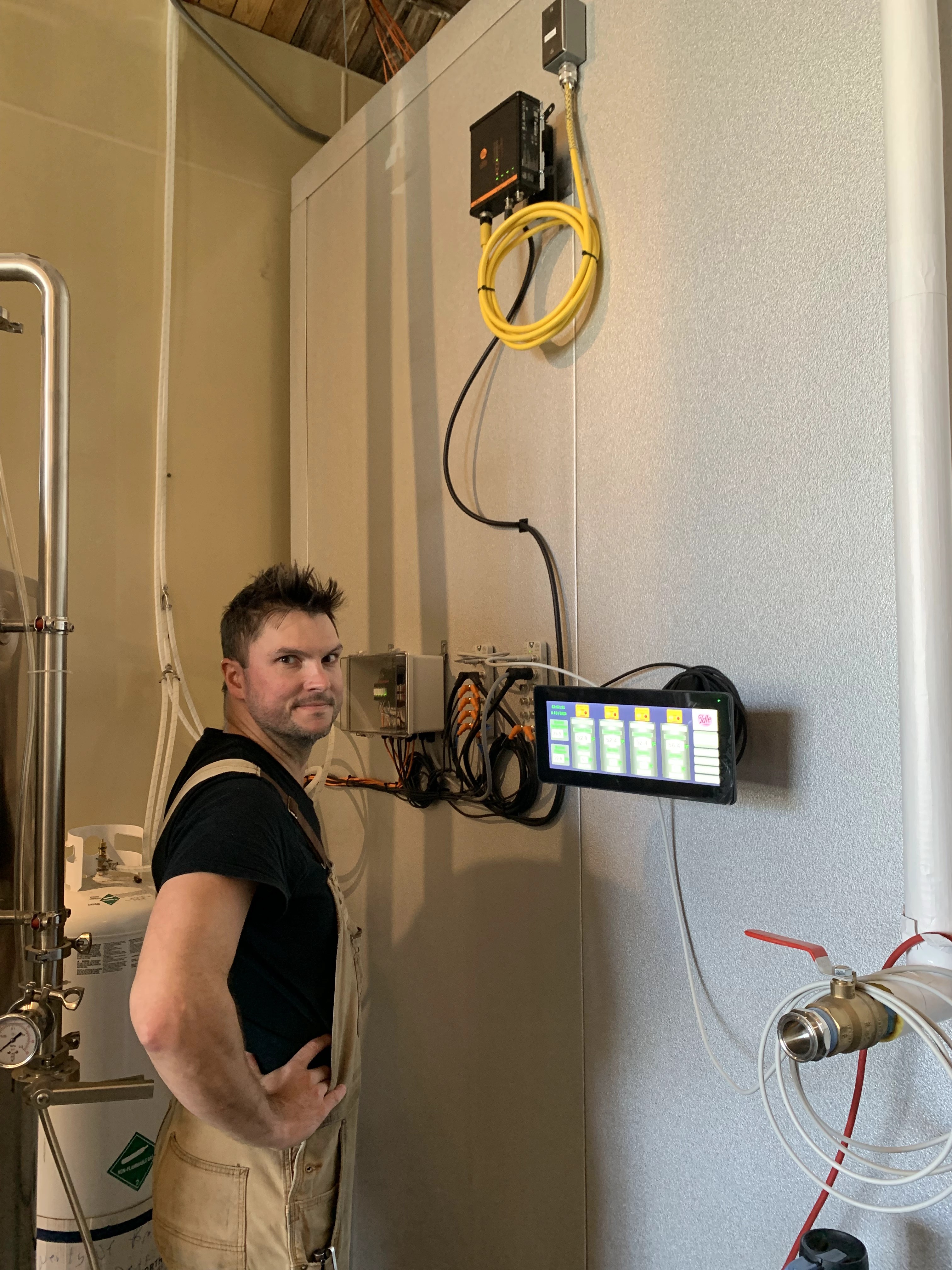 Man beside a wall-mounted HMI screen and control box next to a stainless cellar tank