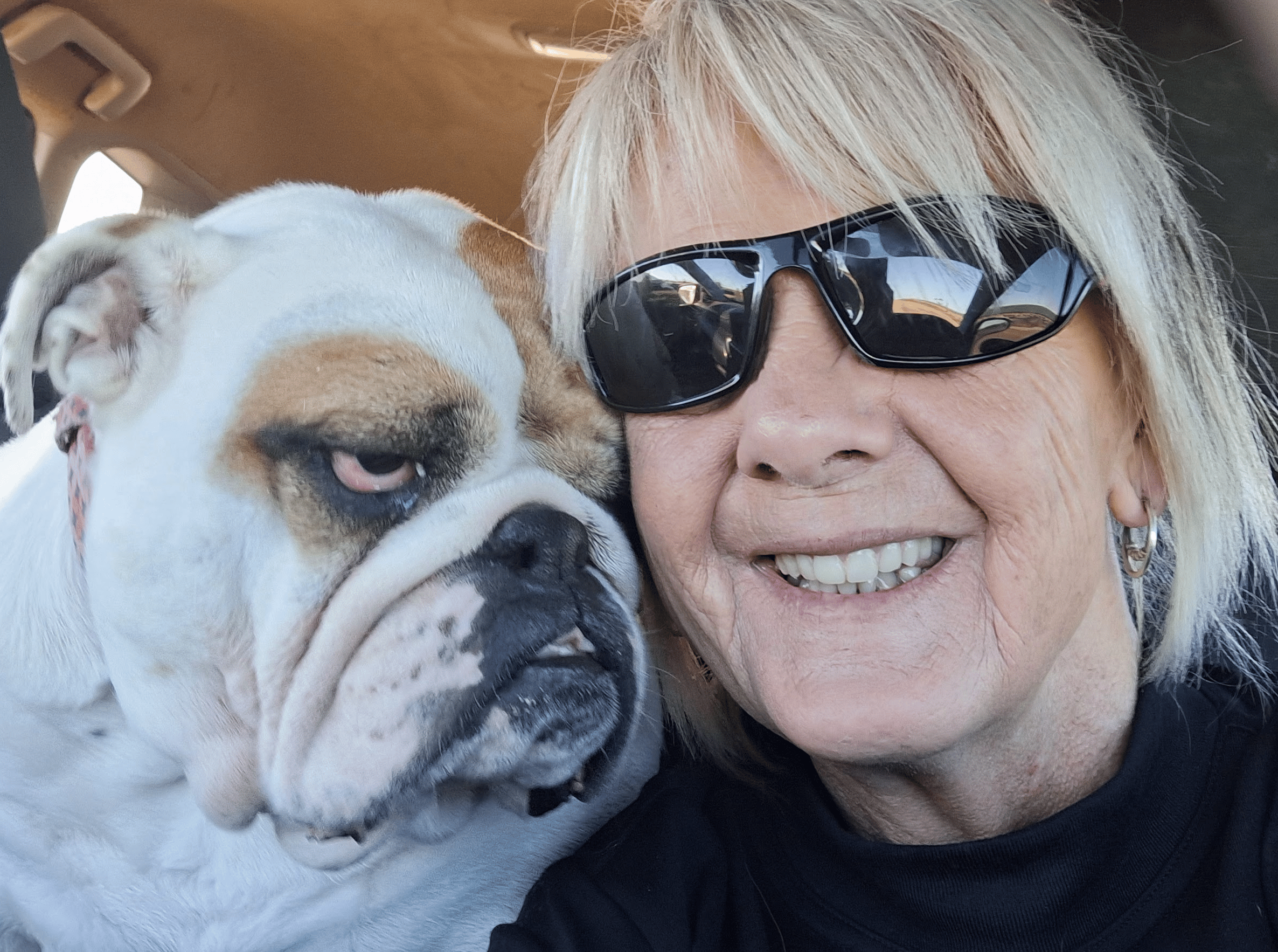 Karen has straight blonde hair and dark sunglasses, she is next to her white bulldog Rosie