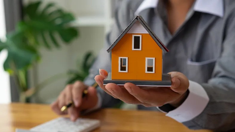 Woman with model house in her hand.