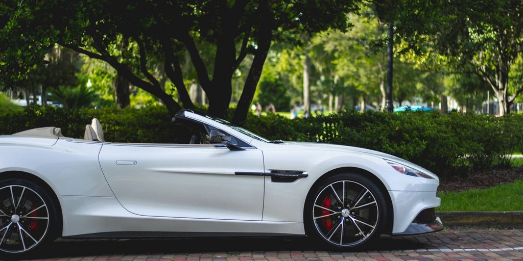 white Aston Martin convertible parked near trees