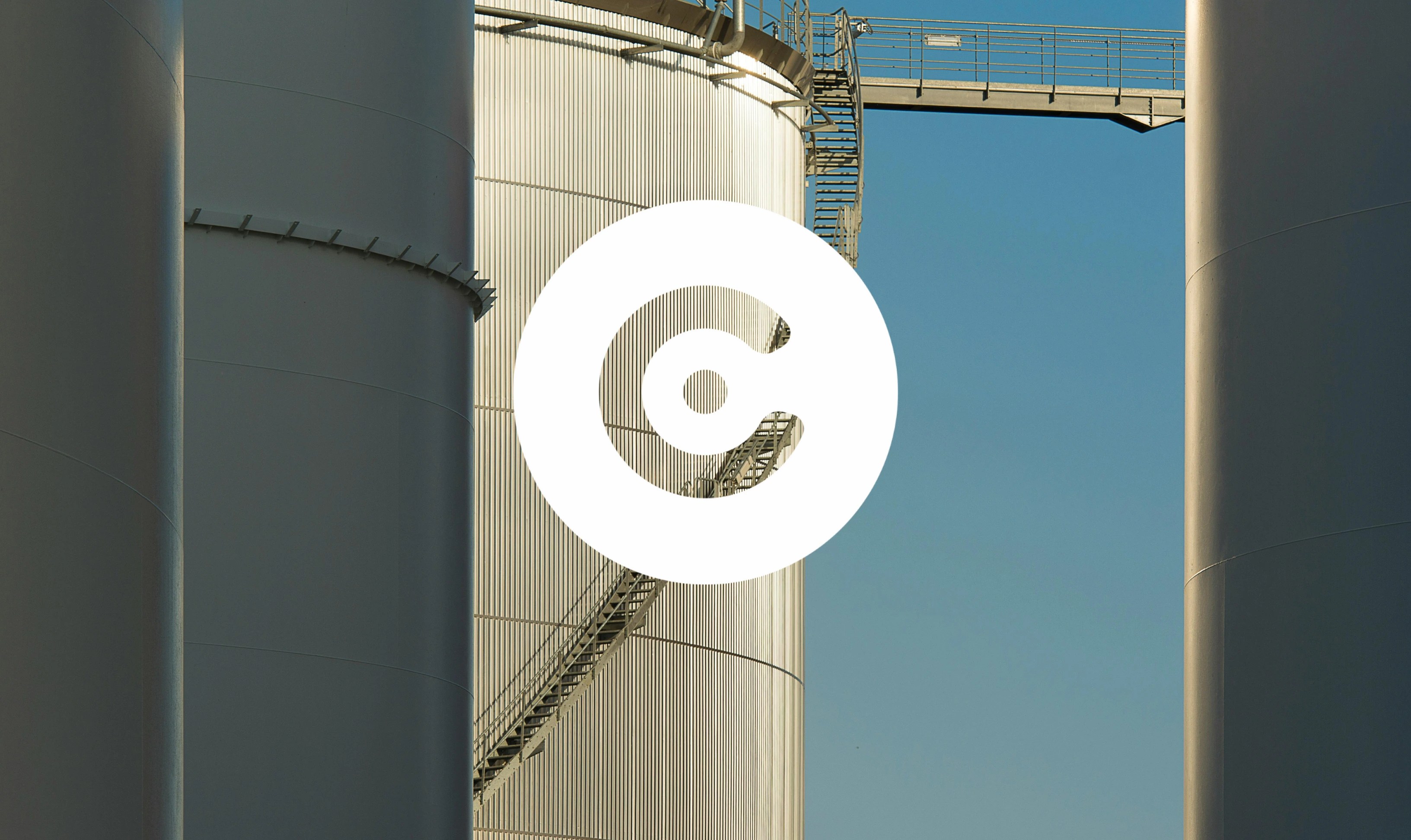 Large industrial storage tanks with metal surfaces and a staircase running along one tank, set against a clear blue sky.