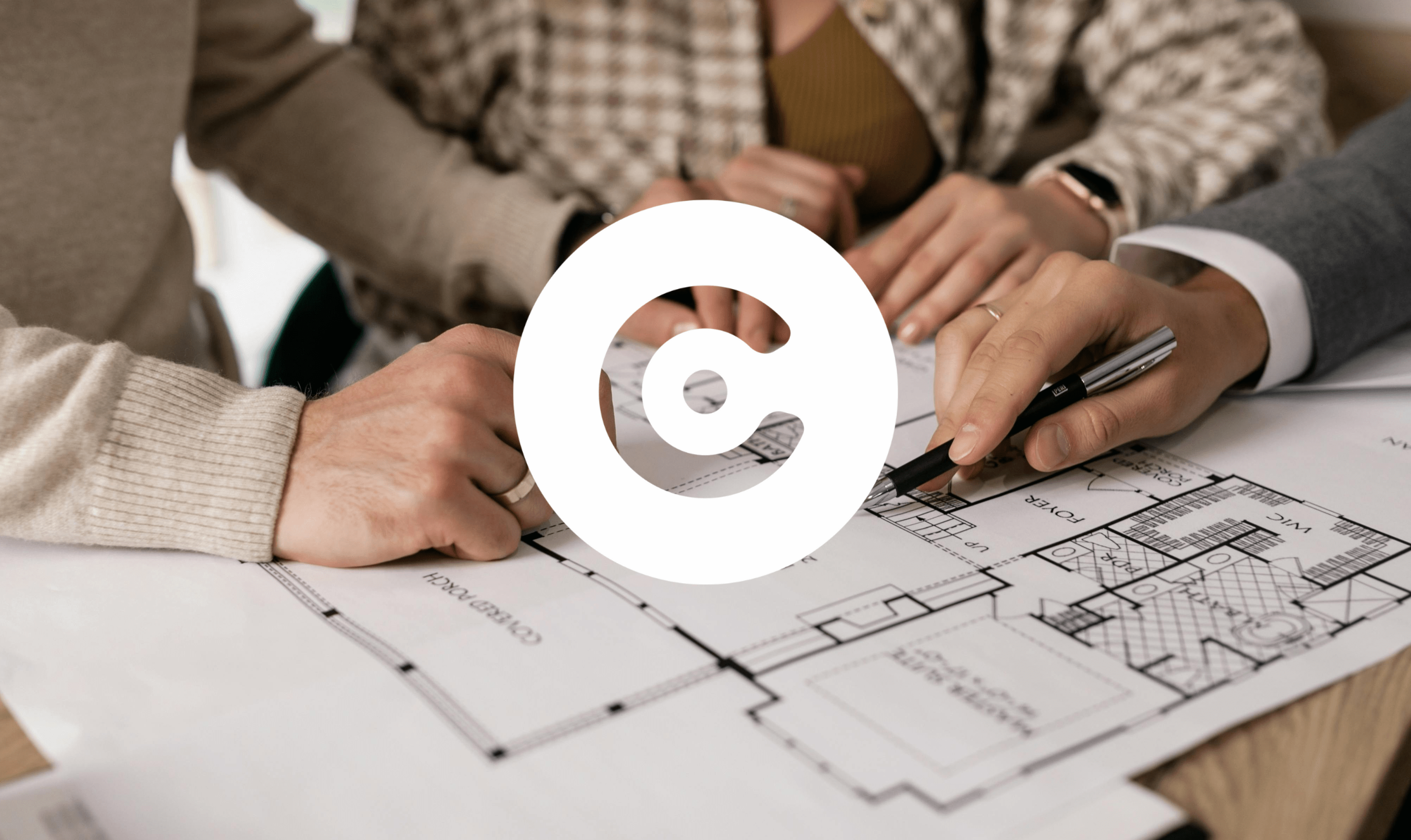 Close-up of people reviewing and pointing at architectural floor plans on a table. A large white circular logo is overlaid in the center.