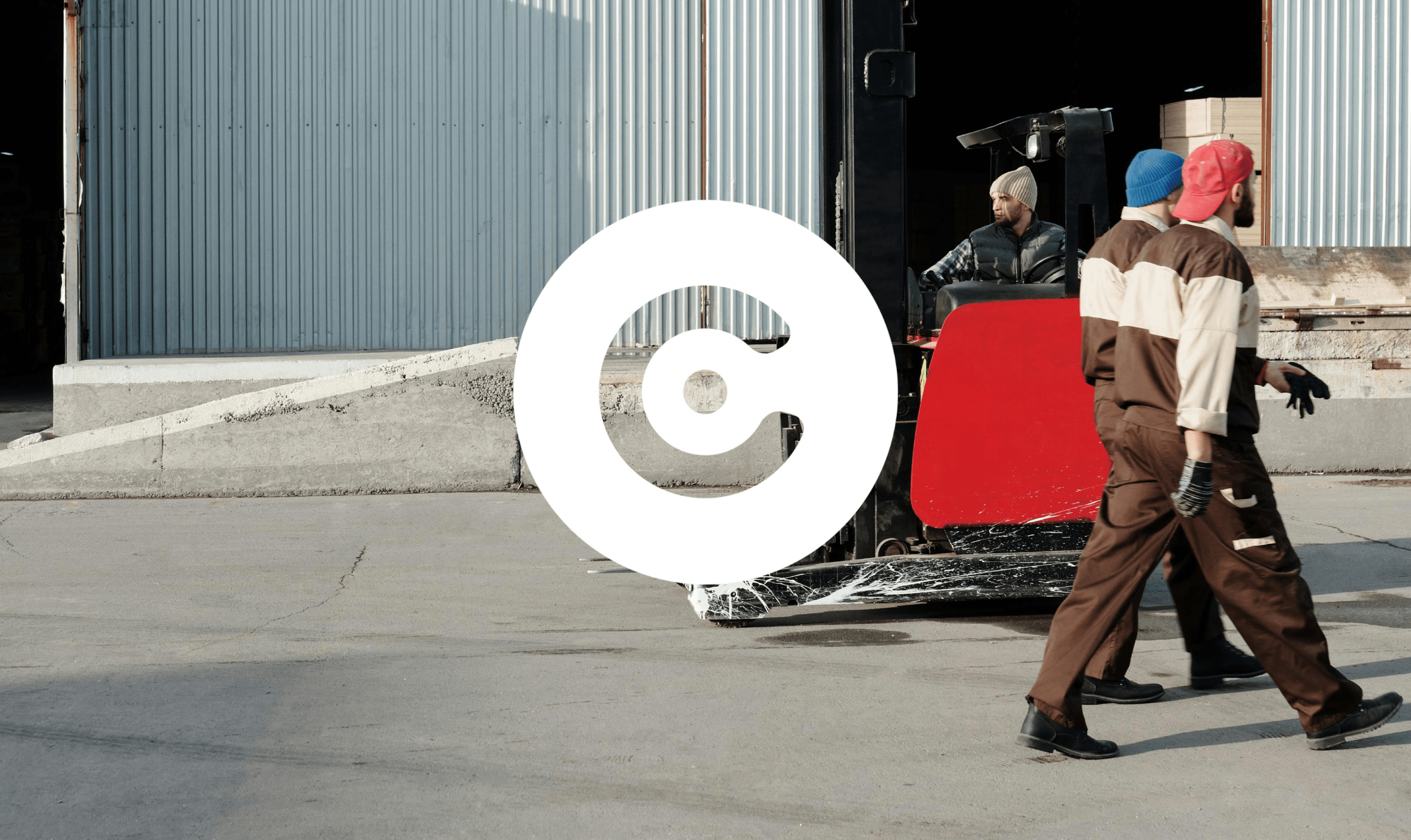 Two workers in brown uniforms walk past a forklift operated by another worker near a warehouse entrance with corrugated metal walls.
