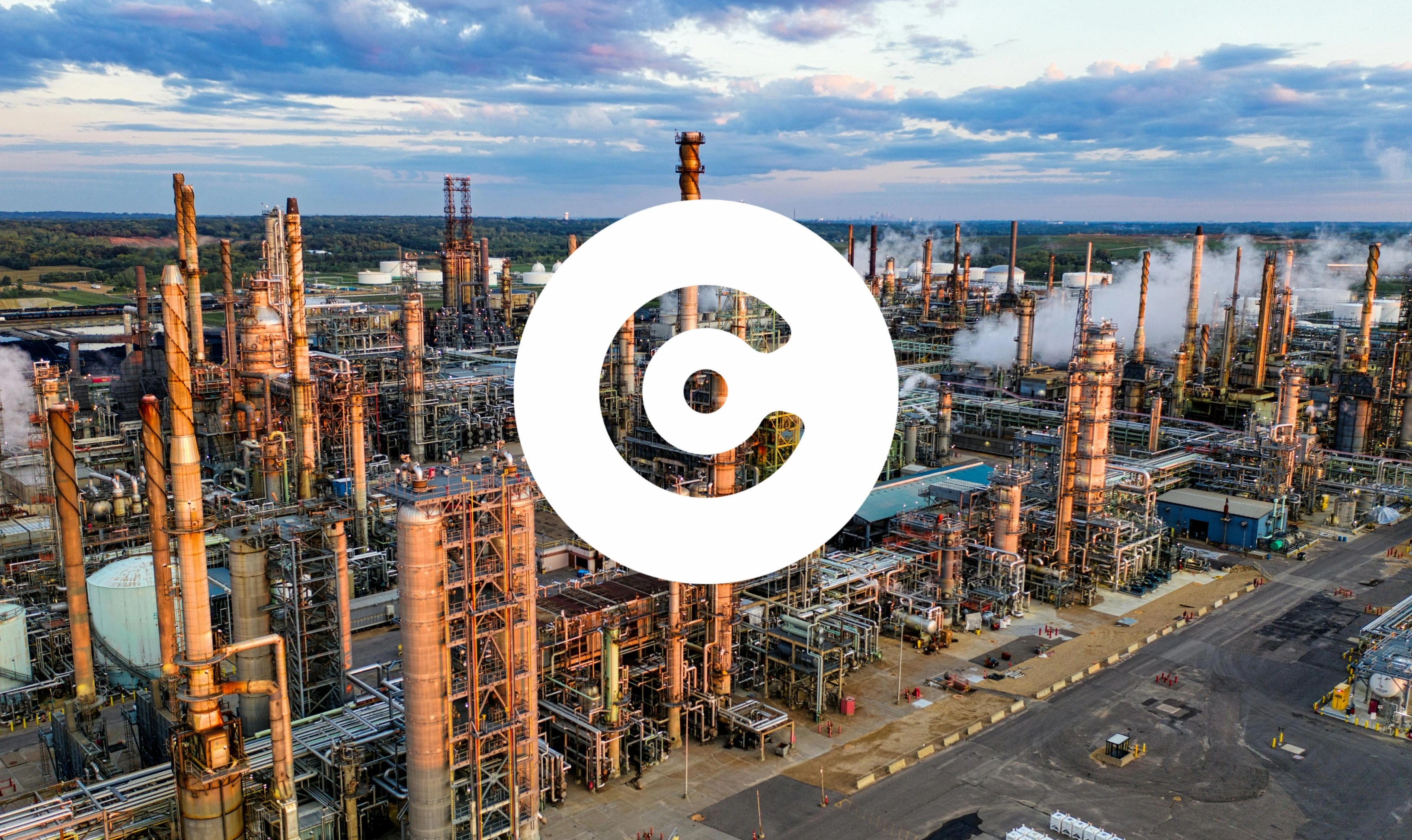 Factory photo with a bold white circular logo with a "C" shape is overlaid in the center of the image.