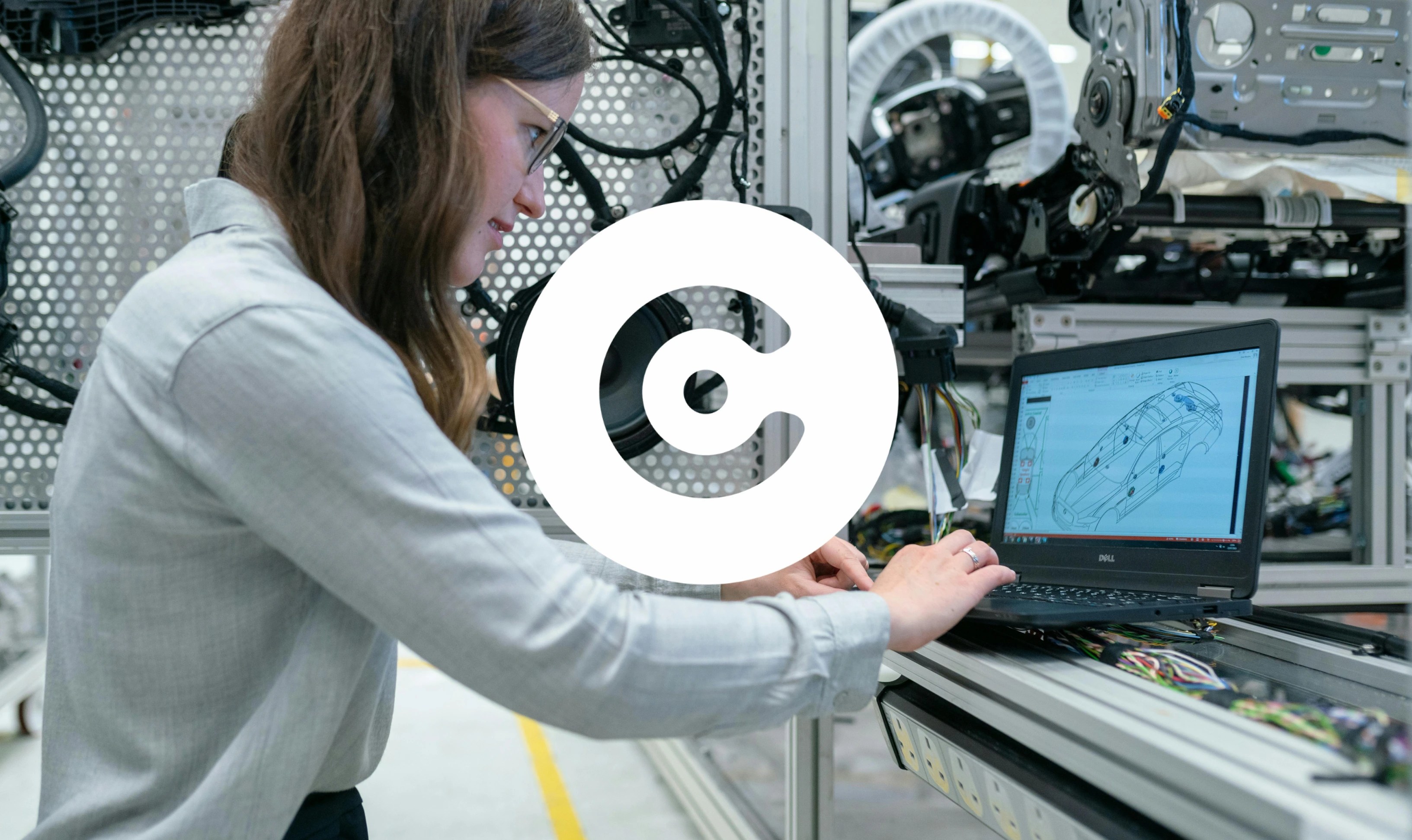 Woman working on a laptop displaying a 3D car model in a manufacturing lab.